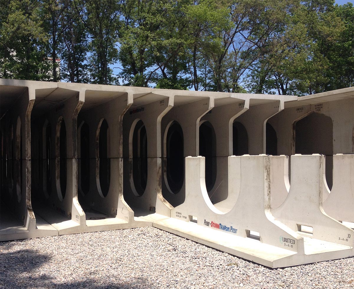 Large concrete tunnel sections are stacked on a gravel lot with trees in the background.