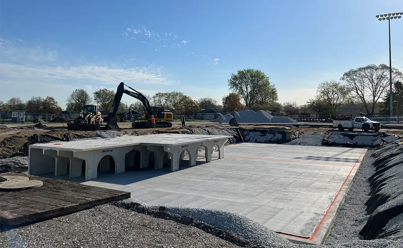 Construction site with heavy machinery and workers installing large precast concrete structures on a prepared foundation under a clear sky.