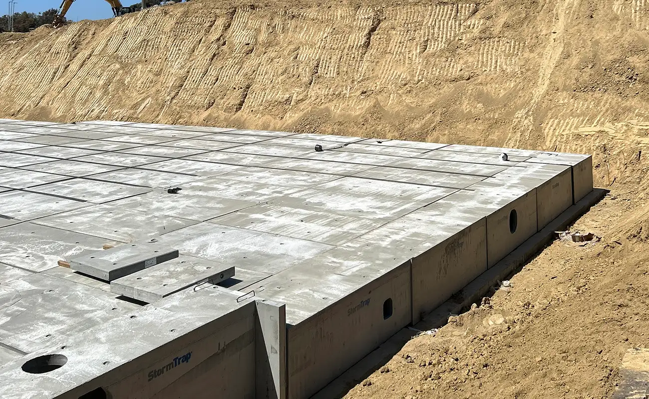 A large, flat concrete slab foundation set in excavated earth at a construction site, with soil embankments in the background.