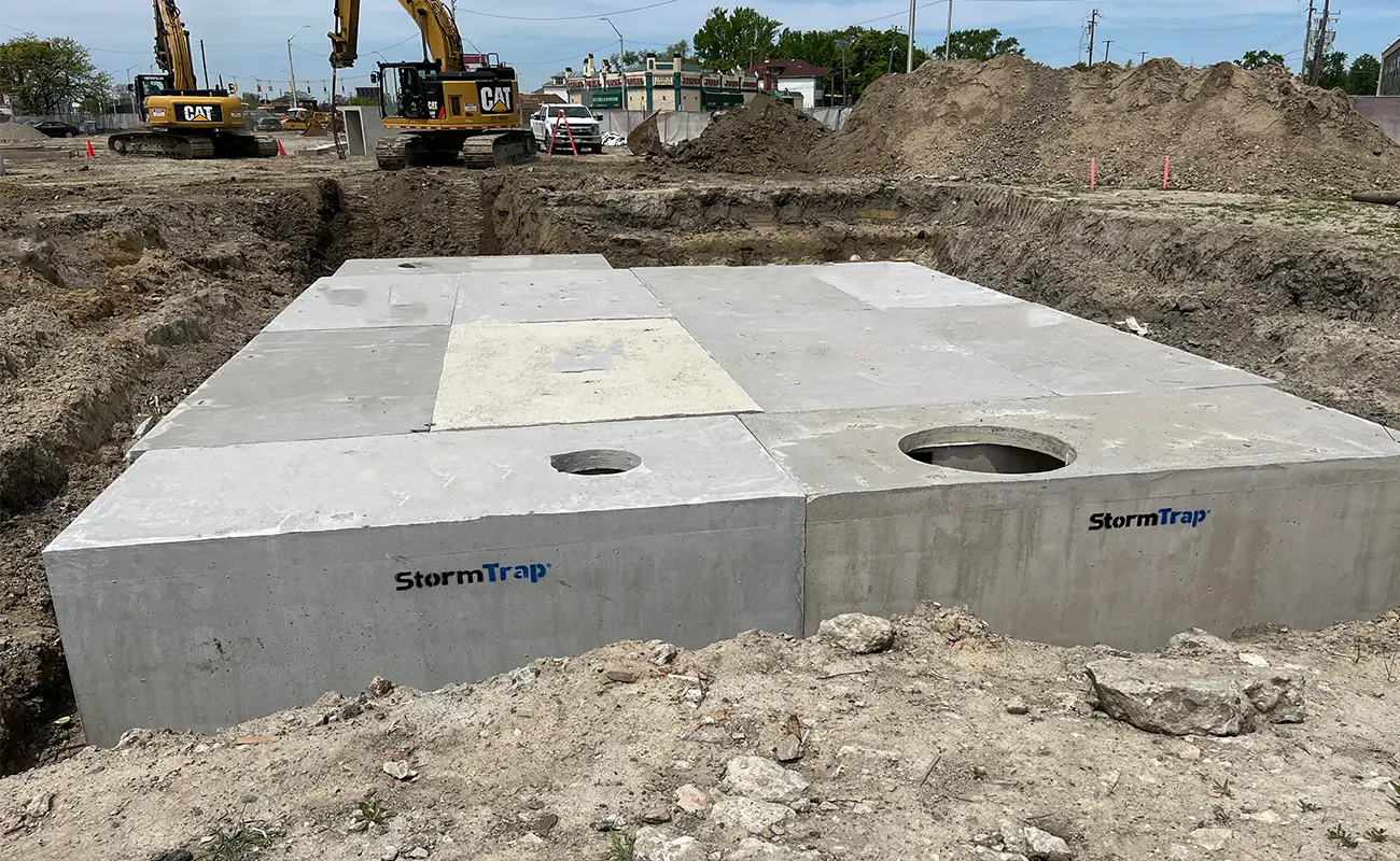 Large concrete StormTrap stormwater management structures are installed in an excavated construction site, with excavators and equipment in the background.