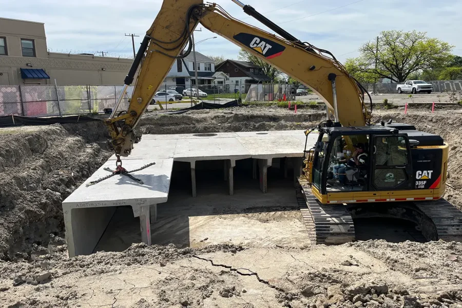 A construction excavator places a large concrete slab over an underground structure at an active construction site.