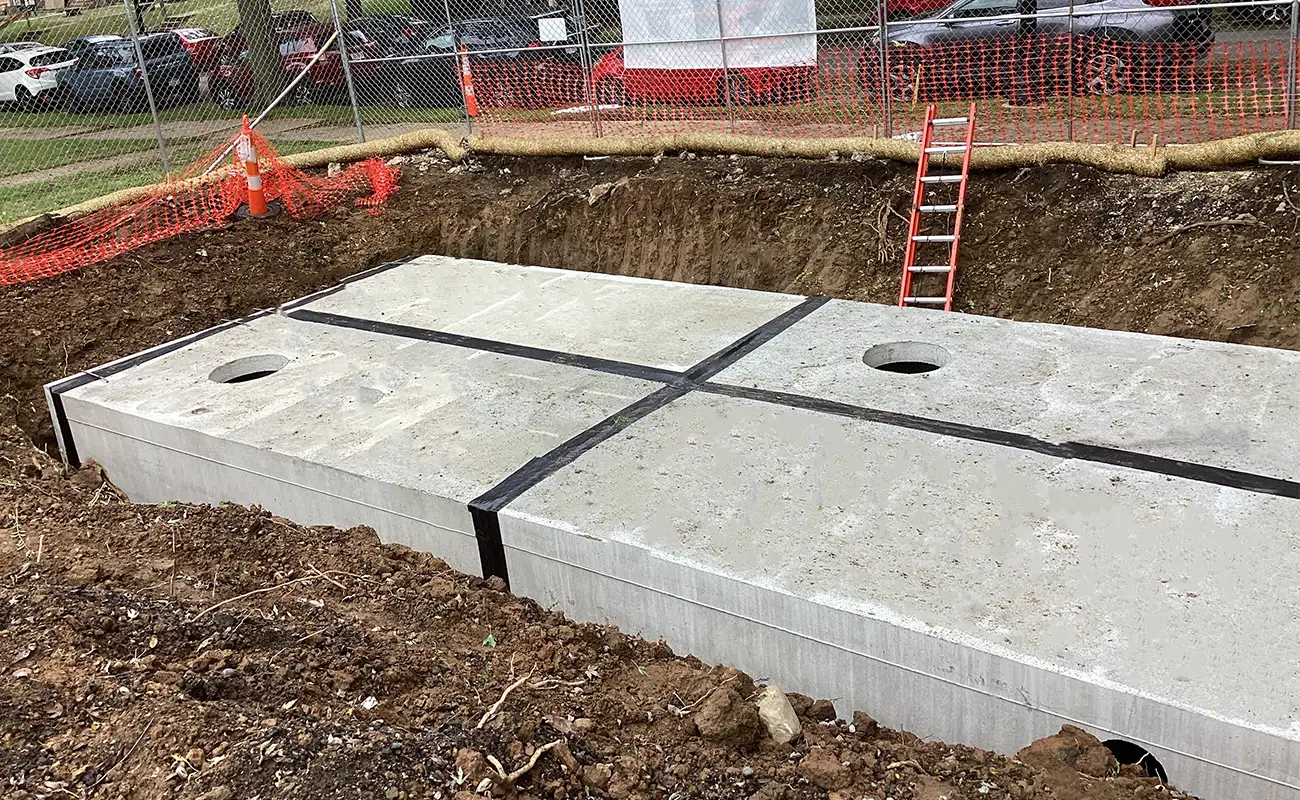 Large concrete vault sections installed in an excavated pit at a construction site, with a red ladder and safety fencing in the background.