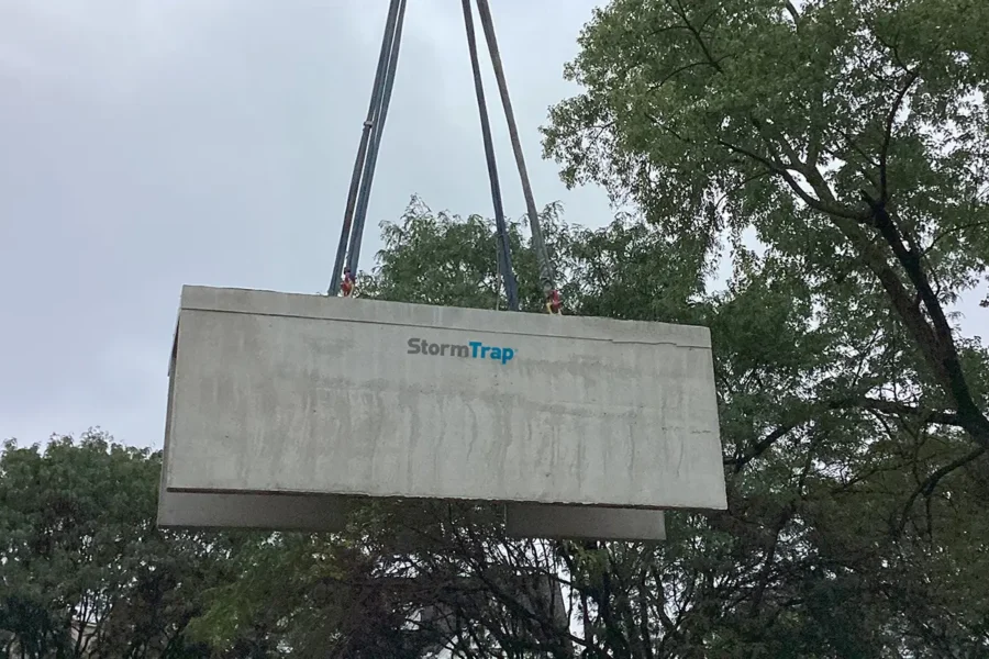 A large concrete StormTrap structure is being lifted by cables, with trees and an overcast sky in the background.