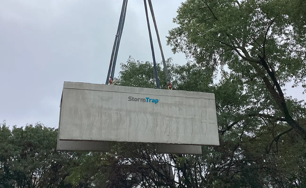 A large concrete StormTrap structure is being lifted by cables, with trees and an overcast sky in the background.