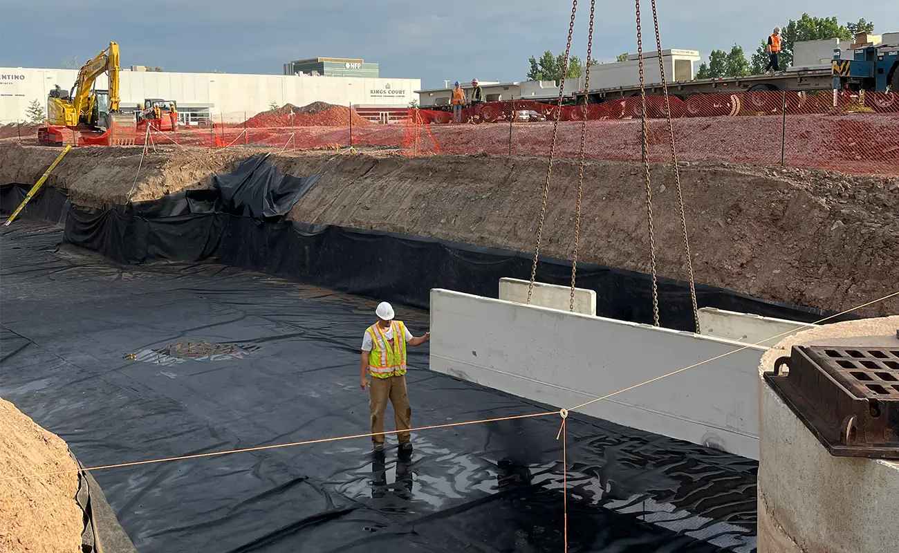 Construction worker guiding first precast concrete DoubleTrap unit into lined excavation at Burlington Ontario stormwater detention project