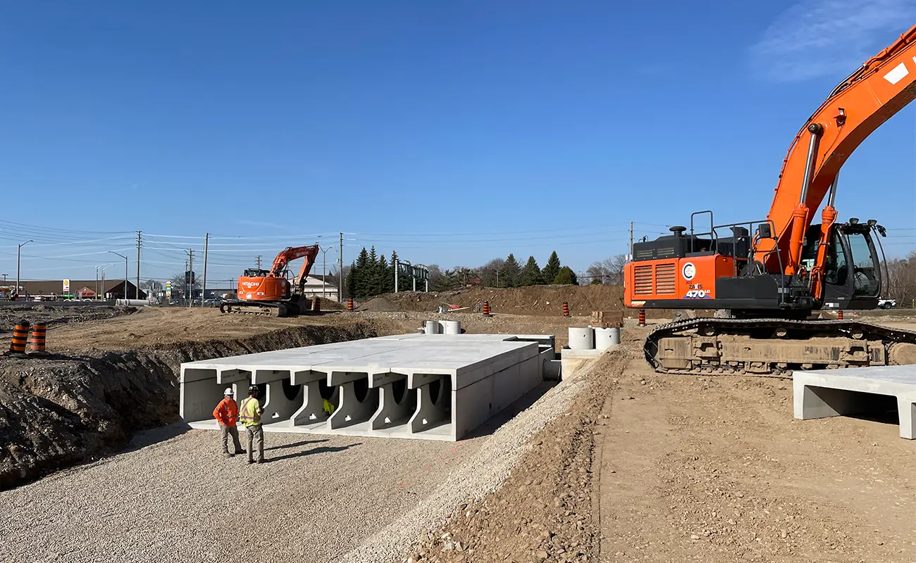 Workers standing beside StormTrap DoubleTrap precast concrete detention units on-site at an industrial warehouse project in Cambridge Ontario