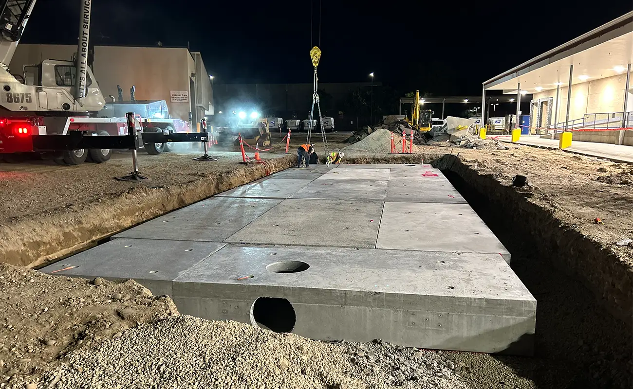 Large concrete slabs being installed in a construction site at night, with workers and vehicles present under artificial lighting.