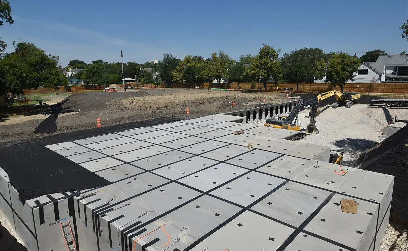 An aerial view of an underground stormwater detention system in University Park, with a yellow excavator working near the large concrete structure.