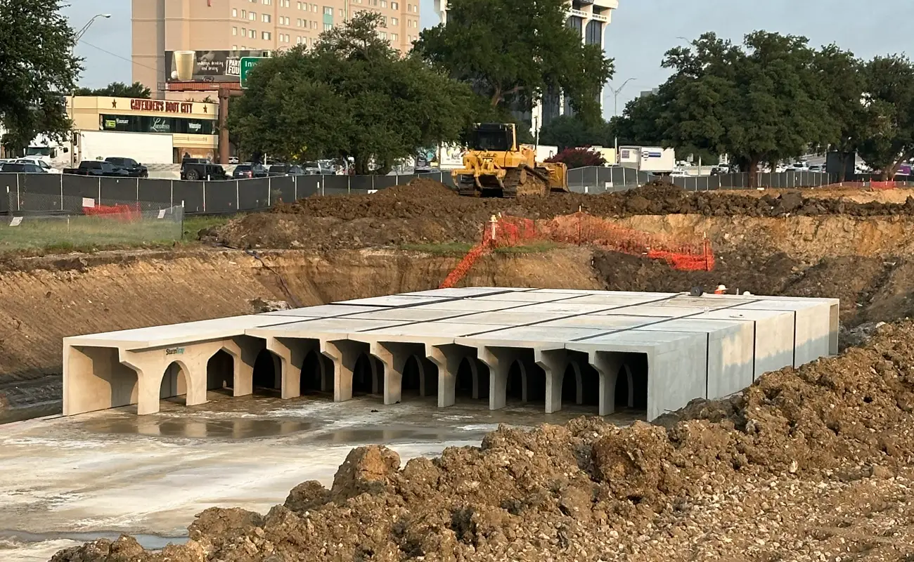 Concrete StormTrap detention system segments installed in an excavated trench at a construction site with a yellow bulldozer in the background.