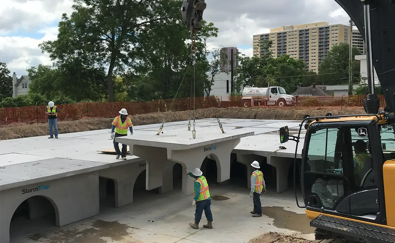 Construction workers guide a crane as it lowers a large precast concrete StormTrap structure, a common stormwater detention system for churches, into place at a building site.